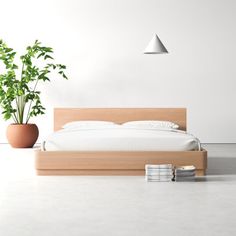 there is a bed with white sheets and pillows on the floor next to a potted plant