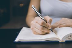 a person is writing on an open book with a pen in their hand while holding a notebook