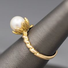 a close up of a ring with a pearl on it's center and gold leaves