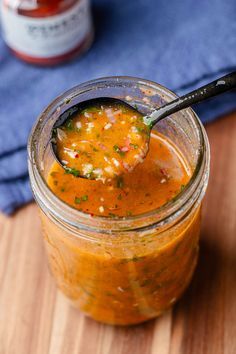 a spoon full of soup sitting on top of a wooden table next to a jar