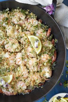 a skillet filled with shrimp, broccoli and lemons on top of a blue table