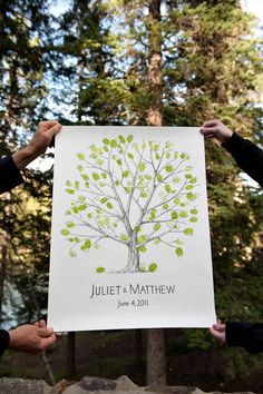 two people holding up a paper with a tree on it in front of some trees