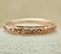 a gold wedding band with flowers and leaves on the side, sitting on top of a rock