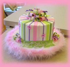 a multi - colored cake decorated with pink, green and purple ribbons on a table