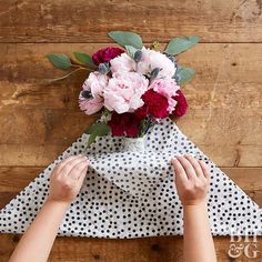 someone is arranging flowers in a vase on top of a polka dot table cloth that has been folded over