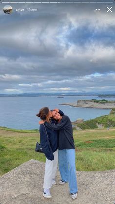 two people standing on top of a rock near the ocean with their arms around each other