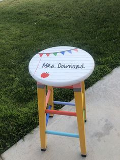 a small wooden stool sitting on top of a sidewalk next to a grass covered field