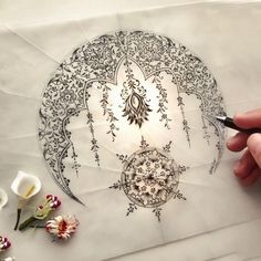 a person drawing on paper with a pen and flower arrangement in the foreground next to it