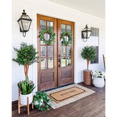 two potted plants are sitting on the front porch with a welcome mat that says welcome