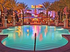 a large swimming pool surrounded by palm trees and tall buildings at night with lights on