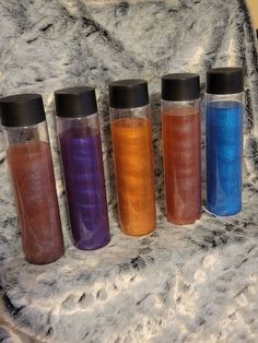 four different colored sand bottles sitting on top of a white fur covered table next to each other