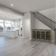 an empty living room and kitchen area with hardwood floors, white walls, and stairs