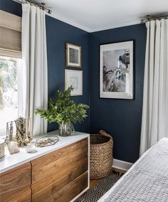 a bedroom with blue walls and white drapes on the windowsill, a large wooden dresser