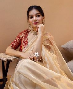 a woman sitting on top of a couch wearing a white sari and gold jewelry