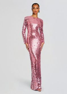 a woman wearing a pink sequin dress with long sleeves and high slits, standing in front of a gray background