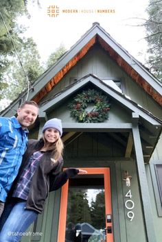 A couple standing in front of an A-Frame cabin. The cabin is painted forrest green with orange trim. The couple is showcasing our modern house numbers in palm springs font, aluminum finish with the numbers 409. There is a wreath above the door. The next 3 images showcases the 409 numbers up close and individually, with an orange modern house numbers logo in the top right hand quarter. Cabin Exterior Colors, Modern Address Numbers, Contemporary House Numbers, Modern House Numbers, Mailbox Numbers, Exterior House Remodel, Mailbox Decals, Houses Exterior