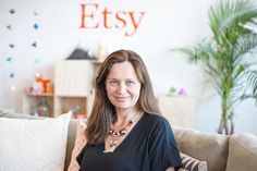 a woman sitting on top of a couch in front of a wall with the word etsy