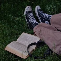 an open book is laying on the grass next to a pair of sneakers