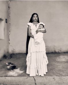 a black and white photo of a woman holding a baby in her arms while standing next to a bird