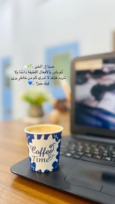 a cup of coffee sitting on top of a laptop computer next to a quote written in arabic