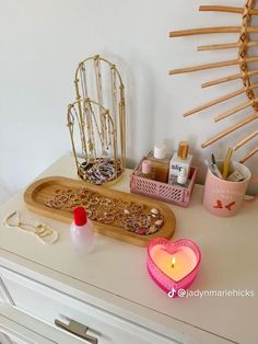 a wooden tray with jewelry on top of a white dresser next to a candle and other items