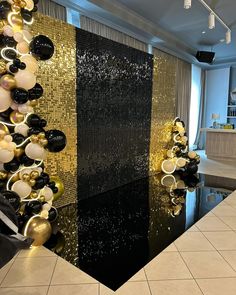 a black and gold room with balloons hanging from the ceiling, in front of a mirror wall