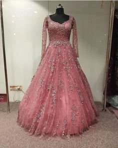 a pink ball gown with long sleeves and beadings on the skirt is displayed in front of a mannequin