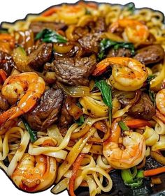 stir fry with beef, noodles and vegetables on a black plate in front of a white background