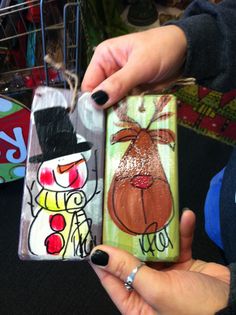 a person holding two small boxes with paintings on them, one is wearing a top hat and the other has a snowman painted on it