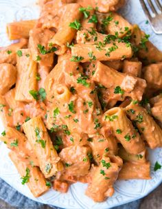 a white plate topped with pasta covered in sauce and parsley next to a fork