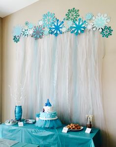 a table topped with cake next to a wall covered in snowflakes and paper flowers