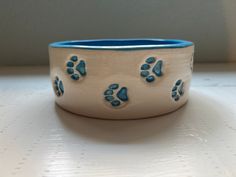 This medium size pet bowl was handmade on the pottery wheel with a smooth white clay and then pressed with this adorable trail of paw prints all the way around it. It is close to 7 inches wide. All blue inside and each paw print hand painted the matching sky blue. They make an excellent water bowl, food bowl or even treats! Also check out the personalized option in my shop! Feel free to message me with any questions or concerns. Dog Pottery Ideas, Dog Bowl Painting Ideas, Pottery Painting Dog Bowl, Pottery Bowls Painting Ideas, Clay Cat Bowl, Clay Dog Bowl, Cat Bowl Pottery, Pottery Beginners, Pottery Dog Bowl