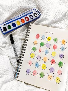 an open notebook with watercolors and markers next to it on a white sheet