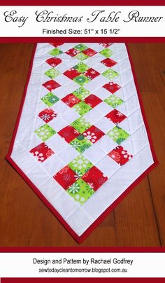 a quilted table runner with red, green and white squares on the top is sitting on a wooden floor