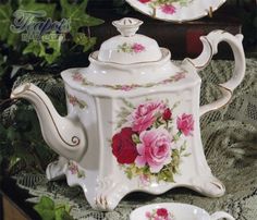 two teapots with roses painted on them are sitting on a lace tablecloth