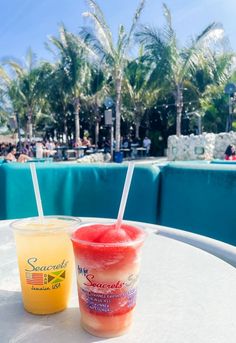 two drinks sitting on top of a table next to each other near a swimming pool