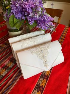 purple flowers are in a vase next to two white napkins on a red tablecloth