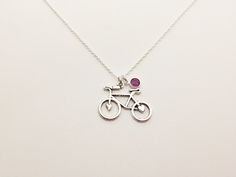 a silver necklace with a bike and a pink stone on it's back end