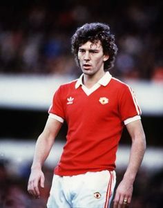 a man in a red shirt and white shorts standing on a soccer field with his head turned to the side