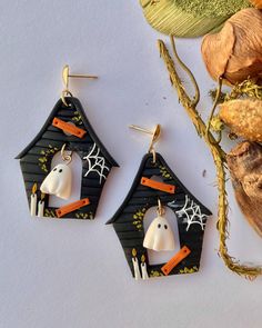 two halloween themed earrings with ghost faces and bats hanging from them, next to dried leaves