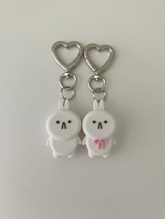 two key chains that are shaped to look like rabbits with bows on their heads and hearts in the background