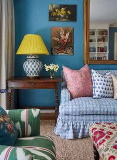 a living room with blue walls and colorful pillows on the couch, coffee table and lamp