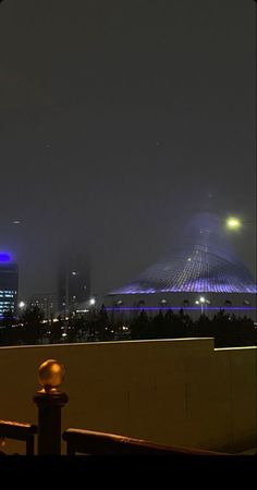 the city skyline is lit up in blue and white lights at night, as seen from an elevated walkway