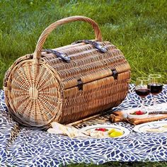 a picnic basket with wine and bread on a blanket in the middle of some grass