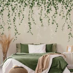 a bed with green sheets and pillows in front of a white wall that has ivy vines on it