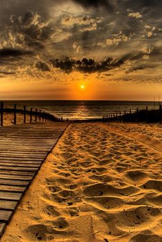 the sun is setting over the beach with sand and wooden walkway leading to the water