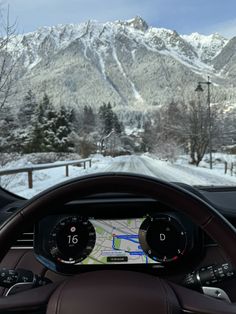 the dashboard of a car driving down a road with snow covered mountains in the background