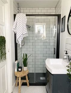 a white and black tiled bathroom with a wooden stool next to the shower door, potted plants on the side