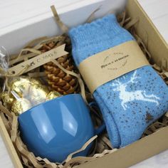 an open box with two blue mugs and socks in it next to some pine cones