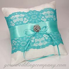 the ring pillow is adorned with a blue ribbon and broochie on it's side